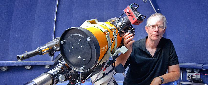 Dr Fred Espenak leans to the right of a large telescope in an observatory.