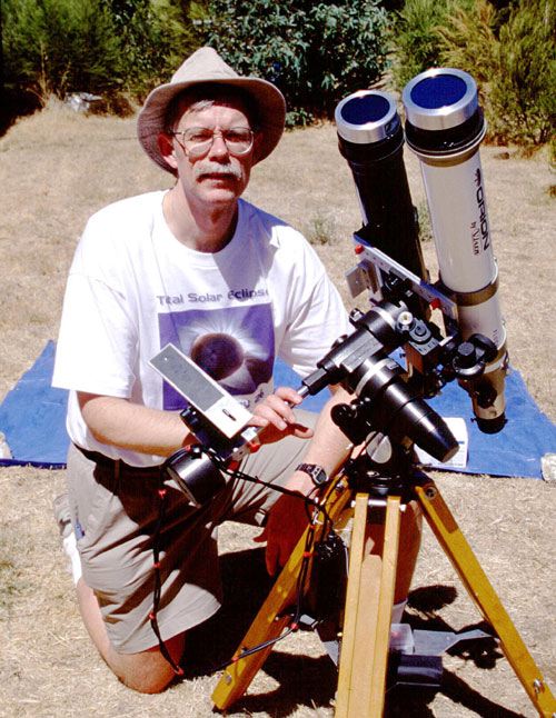 Dr Fred Espenak is kneeling to the left of his solar telescope which is set up outdoors.