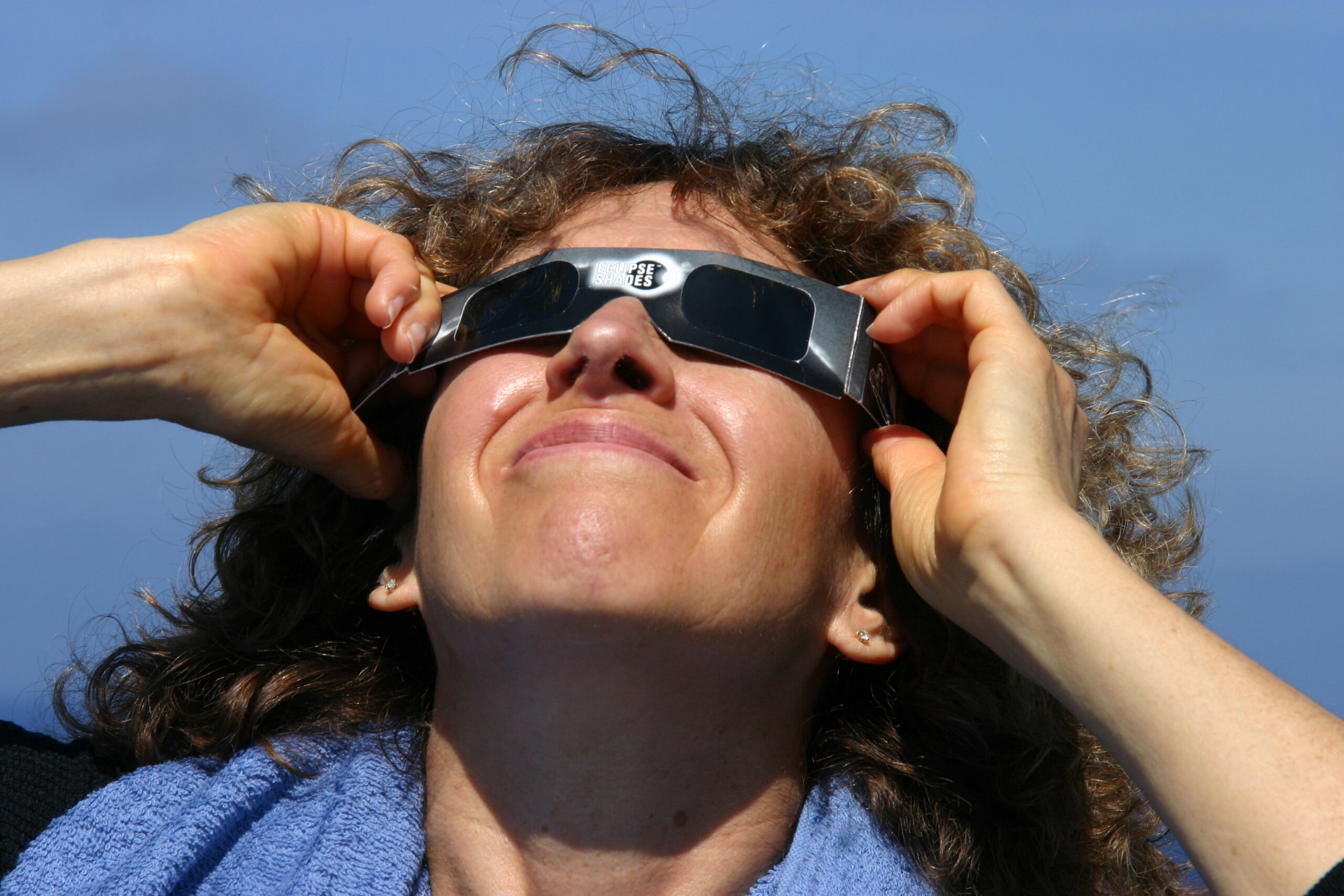 A woman is looking into the sky whilst wearing eclipse glasses.