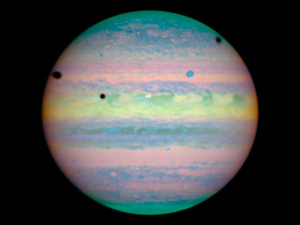 Jupiter, captured from a distance, has three dark circular spots on it. The spots are shadows caused by Sunlight being blocked by Jupiter's Moons.