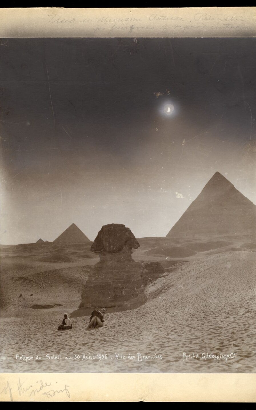 Sandy landscape with Egyption pyramids visible in the background. A woman sits on the Sand as the Moon crosses the Sun.